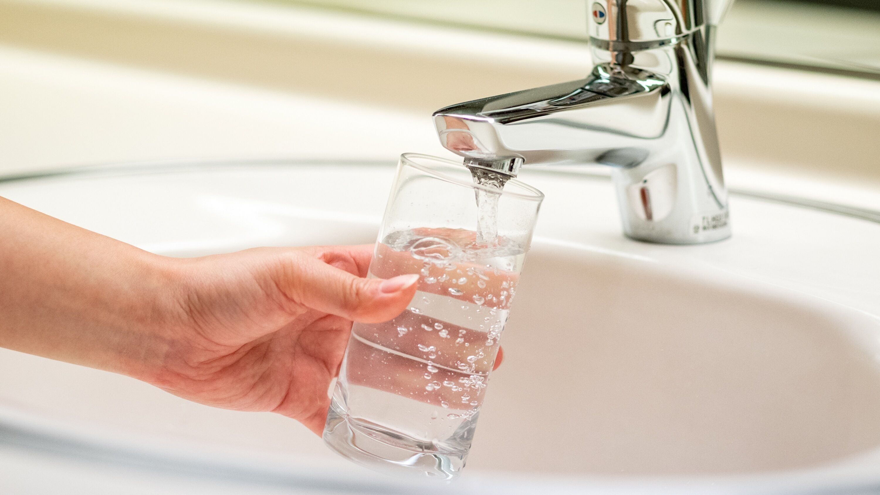 A hand holding a glass of water under a faucet in a sink.