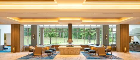 A spacious lobby with a central island, large windows offering a view of the outdoors, and a modern ceiling design.