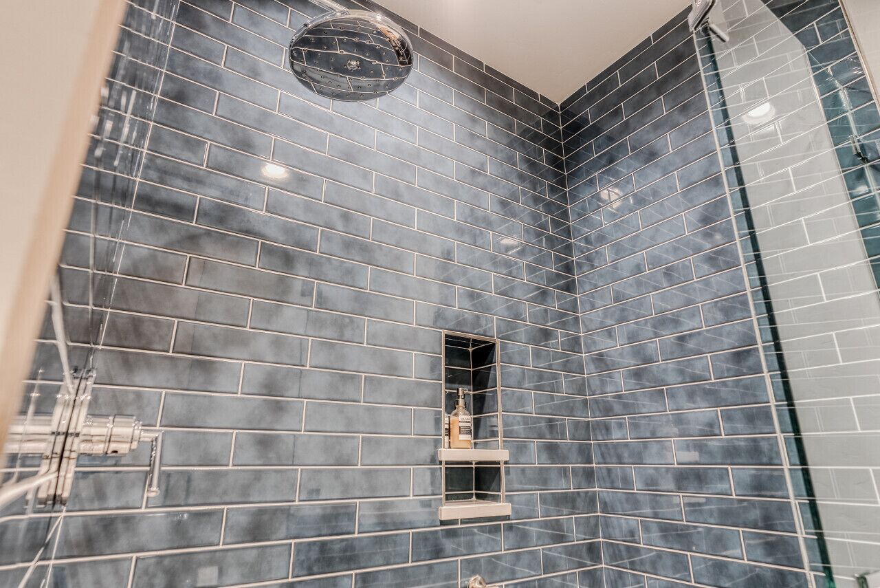 A bathroom with dark blue tiled walls, a glass shower enclosure, and a built-in shelf with toiletries.
