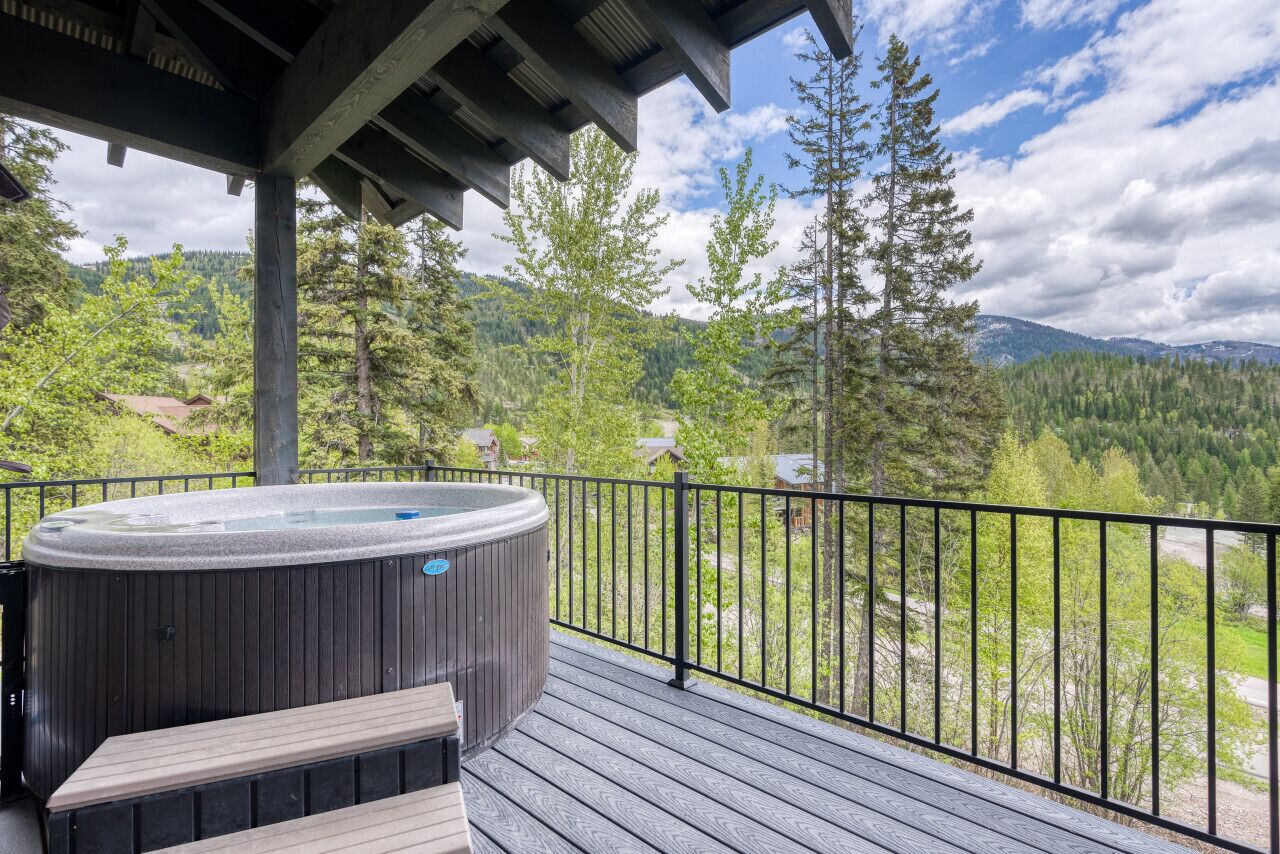 Un bain à remous sur une terrasse en bois, avec vue sur une forêt et des montagnes.