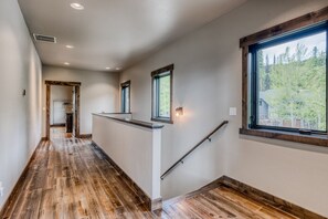 Un pasillo con piso de madera, una escalera con barandilla y una ventana con vista a árboles.