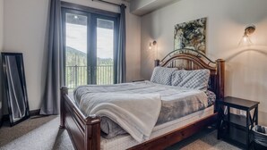 A bedroom with a wooden bed, a view of the outdoors through a window, and a painting on the wall. - Whitefish Mountain Escape, 6 Bedroom Sleeps 14, Amazing Views! (Whitefish)