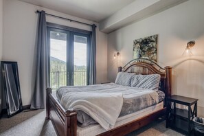 Un dormitorio con cama de madera, vistas al exterior a través de una ventana y un cuadro en la pared.