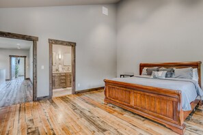 A bedroom with a wooden bed, a wooden floor, and a hallway leading to a bathroom.