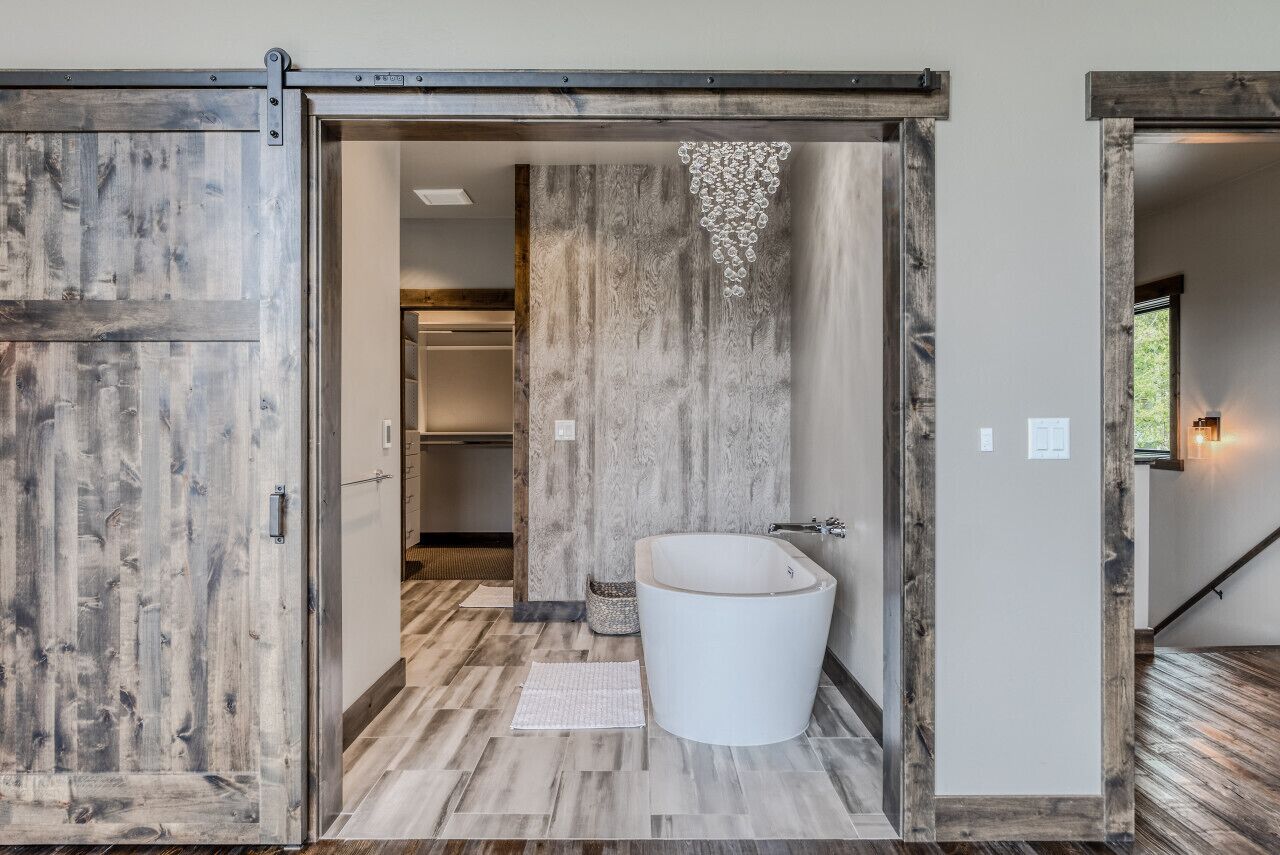 Une salle de bain moderne avec une grande baignoire, un plancher en bois et une porte de style rustique.