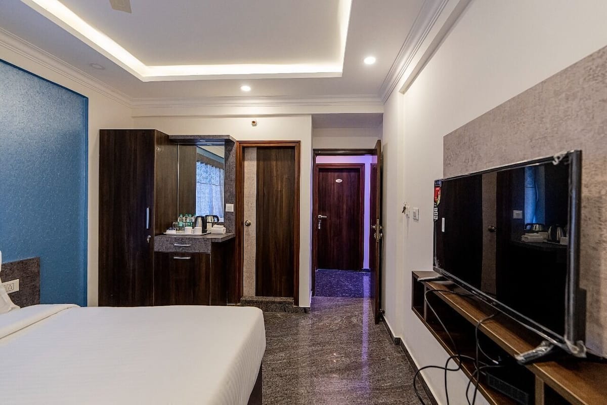 A hotel room with a bed, a TV, a bathroom with a mirror, and a door leading to another room.