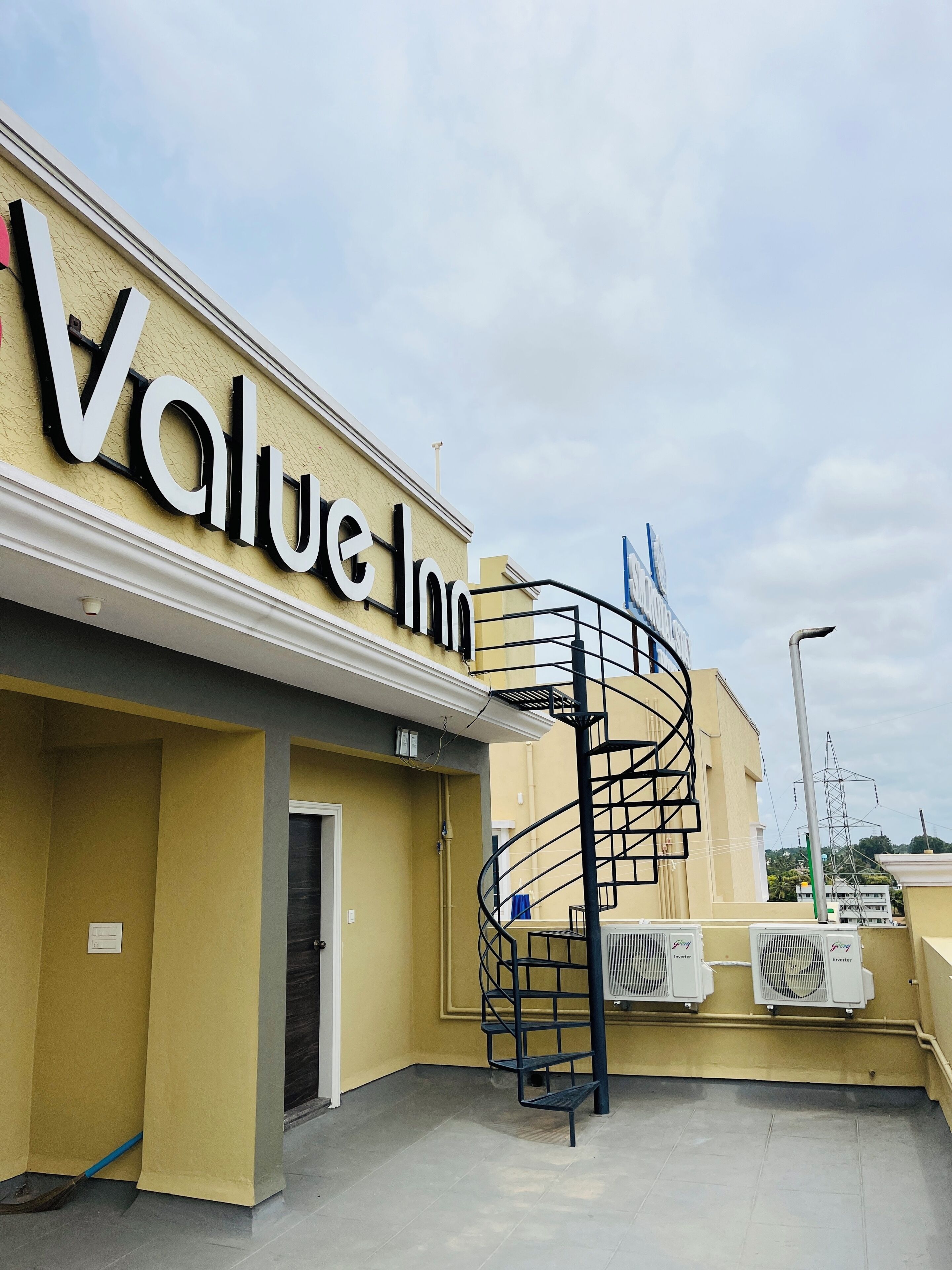 Ein Hotel namens 'Value Inn' mit einer gelben Fassade, einer Wendeltreppe und Klimaanlagen auf dem Dach.