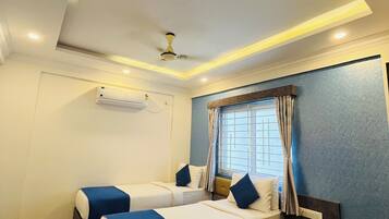 A hotel room with two beds, a ceiling fan, an air conditioning unit, a window with curtains, and a small table with a phone.