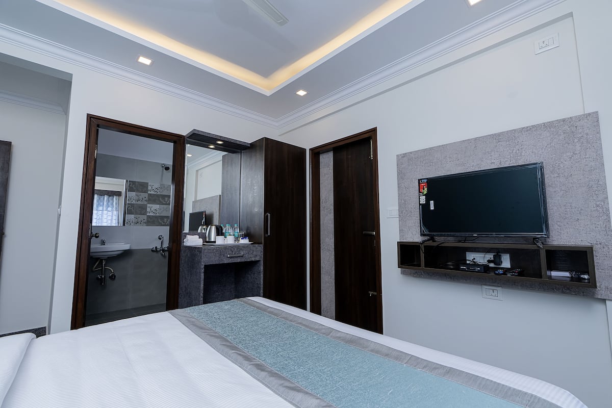 A modern hotel room with a bed, a TV mounted on the wall, a shower area, and a vanity with a sink.