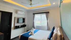 Una habitación de hotel moderna con una cama grande, un ventilador de techo, un televisor de pantalla plana montado en la pared y un ventanal con cortinas.