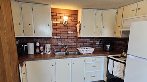 A kitchen with white cabinets, a brick backsplash, and a wooden countertop.