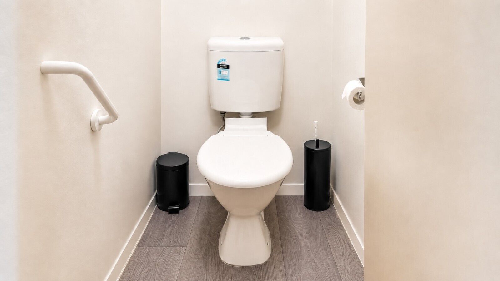 Ein kleines, sauberes Badezimmer mit Toilette, Mülleimer und WC-Bürste.