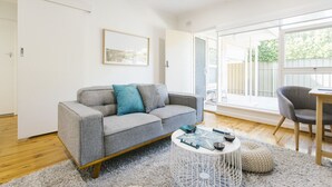 A modern living room with a grey sofa, a round coffee table, and a large window offering a view of the outdoors. - 2 BR Apt | Free Parking & Wi-Fi Near Glenelg Beach (Glenelg East)