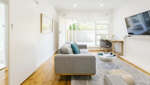 A modern living room with a grey sofa, a coffee table, and a TV mounted on the wall. - 2 BR Apt | Free Parking & Wi-Fi Near Glenelg Beach (Glenelg East)