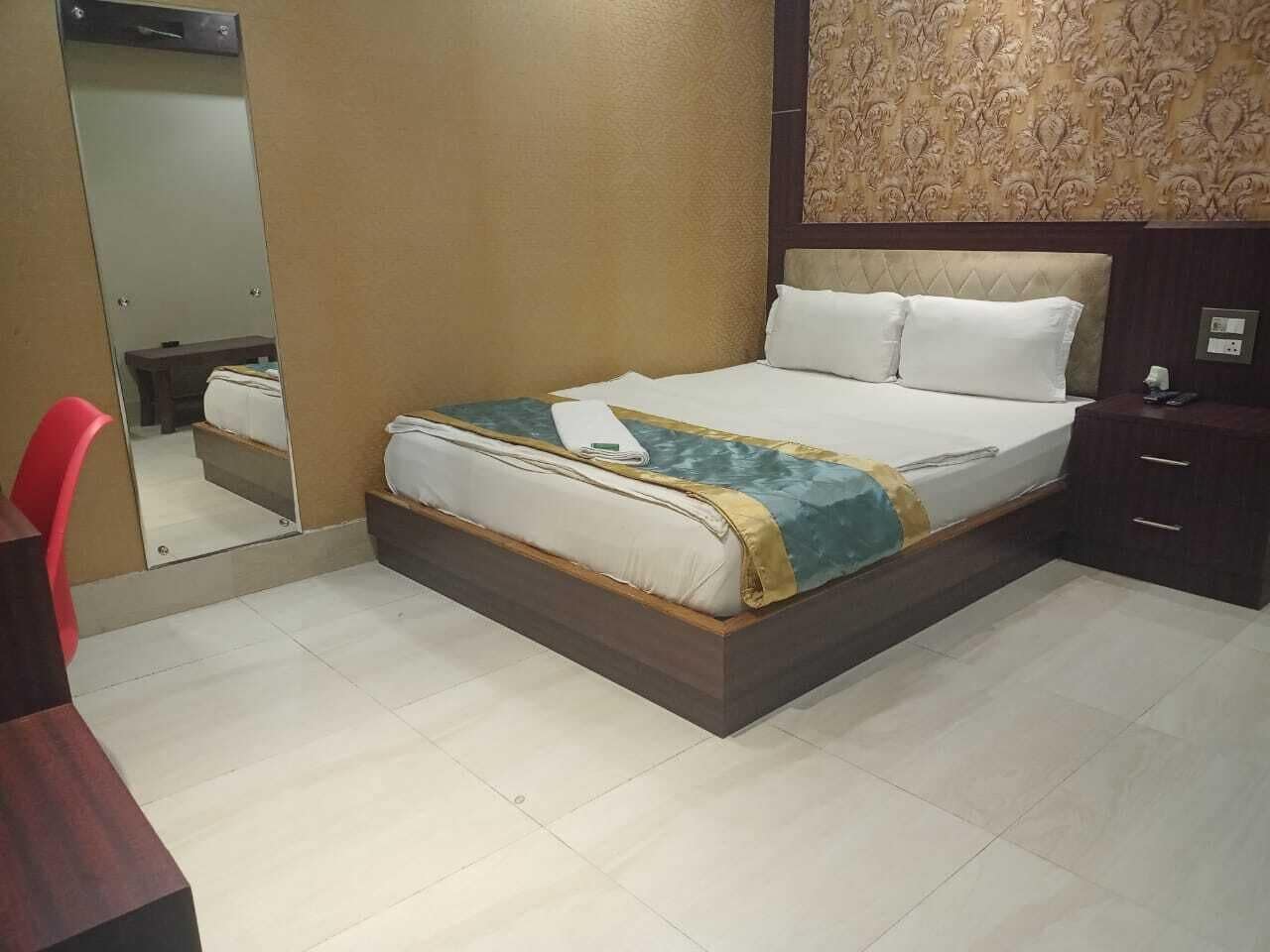 A hotel room with a bed, a bedside table, a mirror, and a wall with a decorative pattern.
