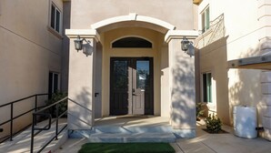 A building entrance with a dark door, a white archway, and a small green area in front. - Hope Hostel 18 Bedroom Christian Setting (Perris)