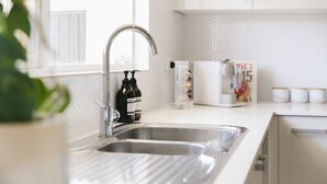 A kitchen with a stainless steel sink, a bottle of dish soap, and a magazine rack with a magazine titled 'MIE'S'.