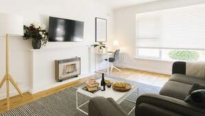 A modern living room with a flat-screen TV, a fireplace, a desk with a chair, and a sofa.