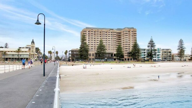 A coastal promenade with a beach, a high-rise hotel, and a pedestrian walkway.