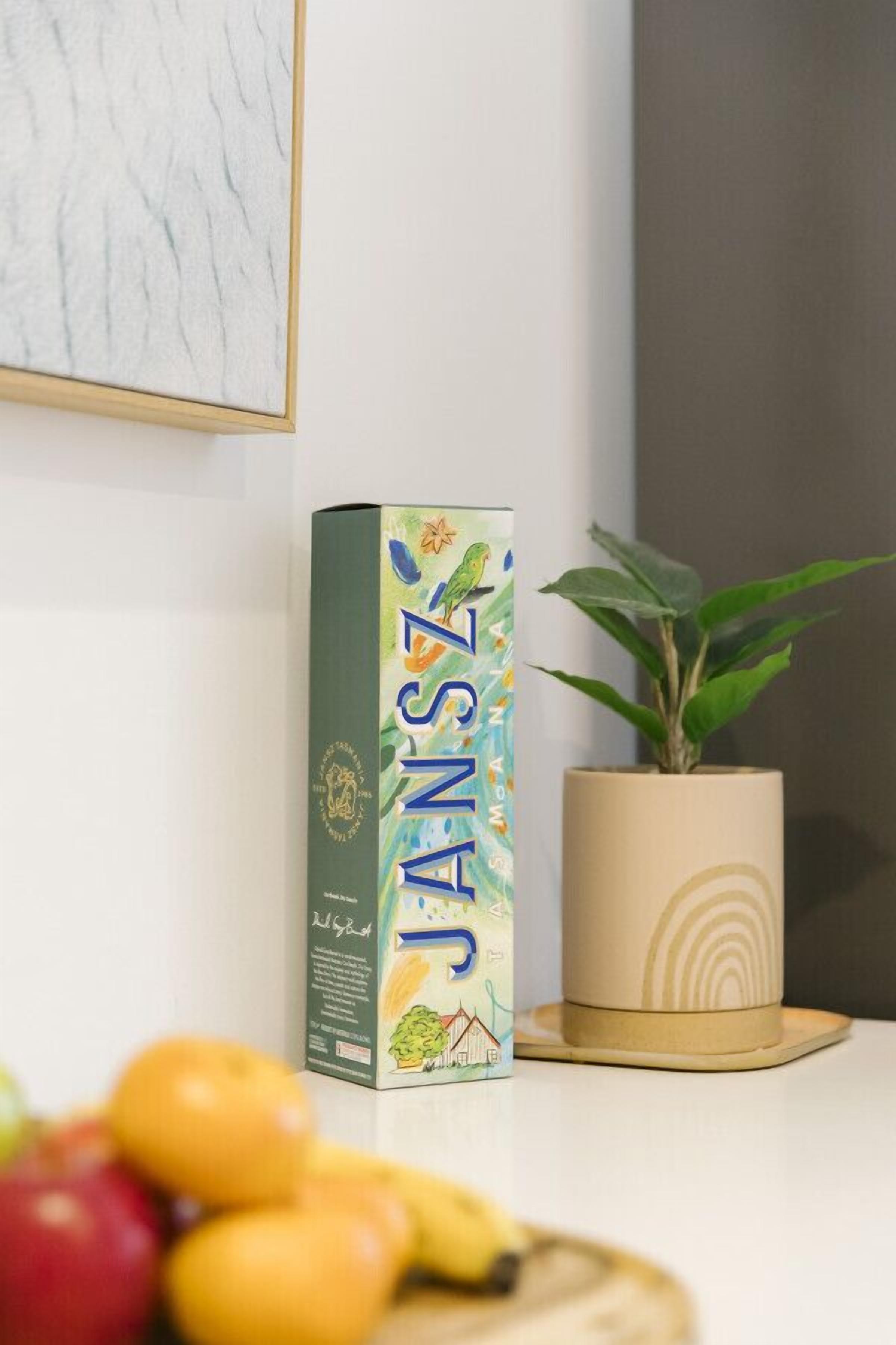 Janssen juice i en kasse, en potteplante og noget frugt på et bord.