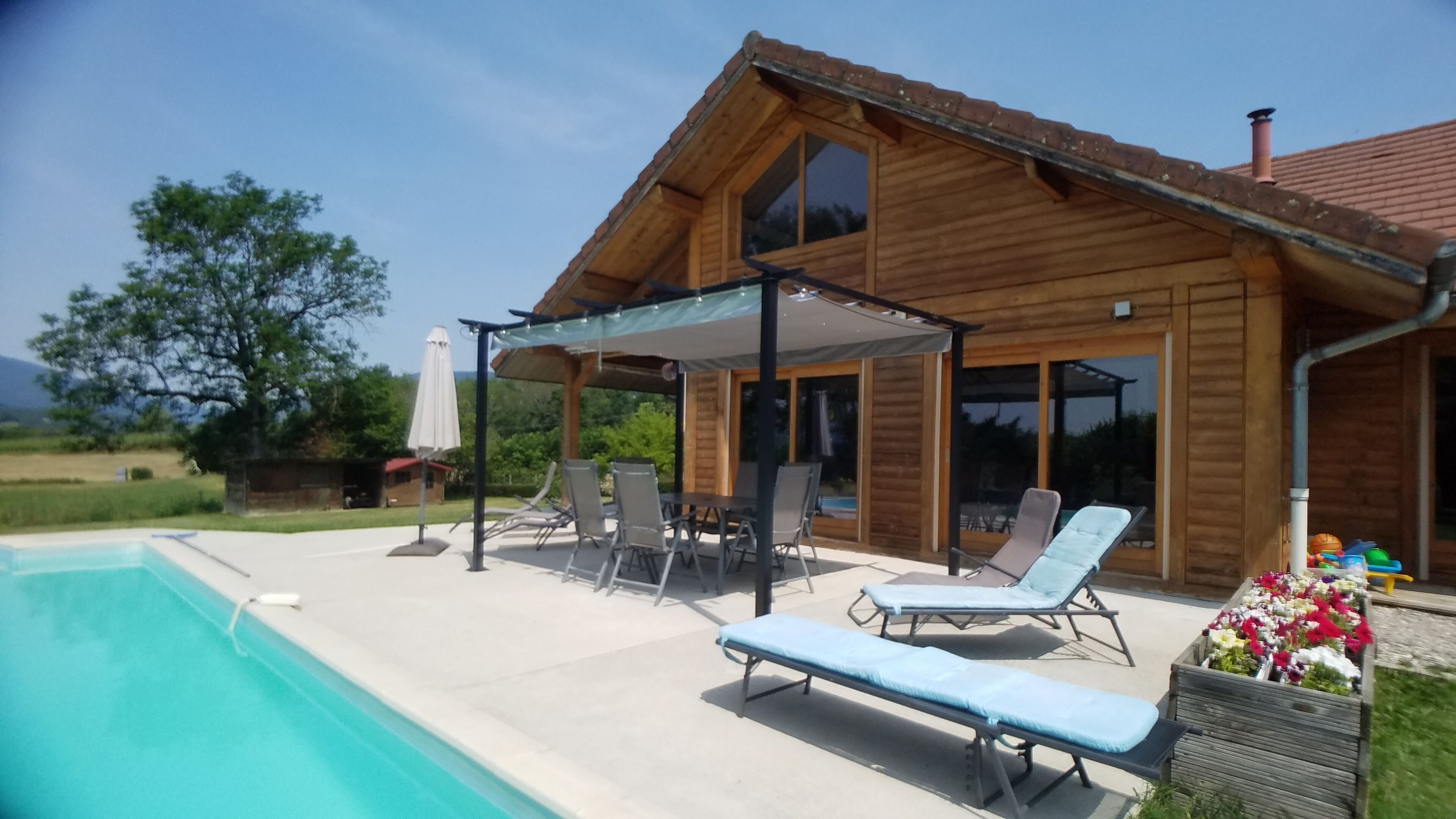 Ein Holzhaus mit Schwimmbad, Sitzgelegenheiten im Freien und einer überdachten Terrasse.