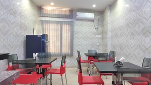 Un comedor con sillas rojas y mesas negras, un ventilador de techo y un equipo de aire acondicionado.