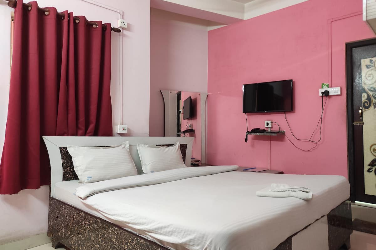 A bed with white linens, a television mounted on the wall, and a red curtain.