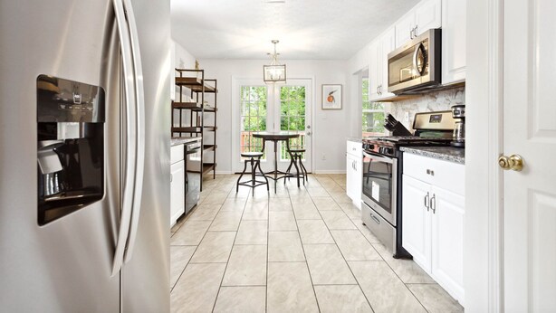 Una cocina moderna con armarios blancos, un refrigerador de acero inoxidable, horno empotrado y comedor con mesa y sillas.