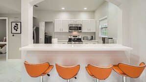 A modern kitchen with white cabinets, a central island with bar stools, and a stainless steel refrigerator. - Superb White Modern Farm House (Austin)