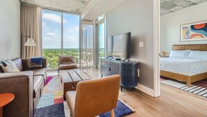 A modern hotel room with a balcony, a bed, a TV, and a seating area with a view of the outdoors. - Modern Downtown Condo*Rooftop pool*Top Amenities (Austin)