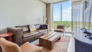 A modern living room with a leather sofa, a wooden coffee table, and a view of a green landscape through large windows. - Modern Downtown Condo*Rooftop pool*Top Amenities (Austin)