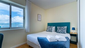 Hotellihuone, jossa on sänky, ikkuna, josta on näkymä, yöpöytä lampun kanssa ja seinällä oleva kehystetty kuva.
