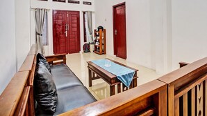 A living room with a sofa, a wooden coffee table, and two red doors. - OYO LIFE 92034 Jay Homestay Syariah (Bandar Lampung)