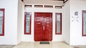 A red door with a metal gate, a tiled entrance, and a small mat. - OYO LIFE 92034 Jay Homestay Syariah (Bandar Lampung)