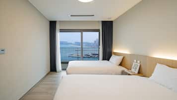 A hotel room with two beds, a view of the city through large windows, and a balcony with a railing.