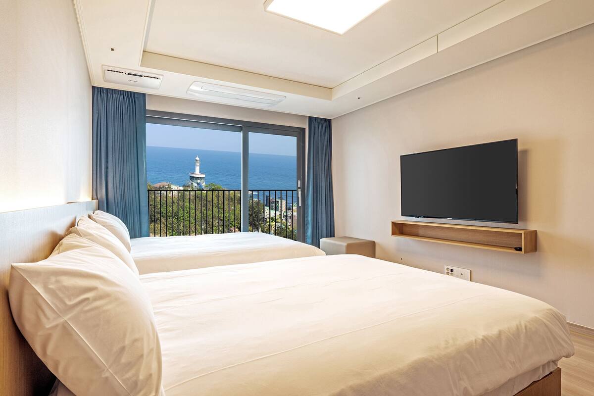 Habitación de hotel con dos camas, televisor y balcón con vista al mar.