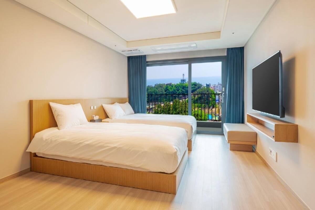 Habitación de hotel con dos camas, televisión y balcón con vistas a la ciudad.