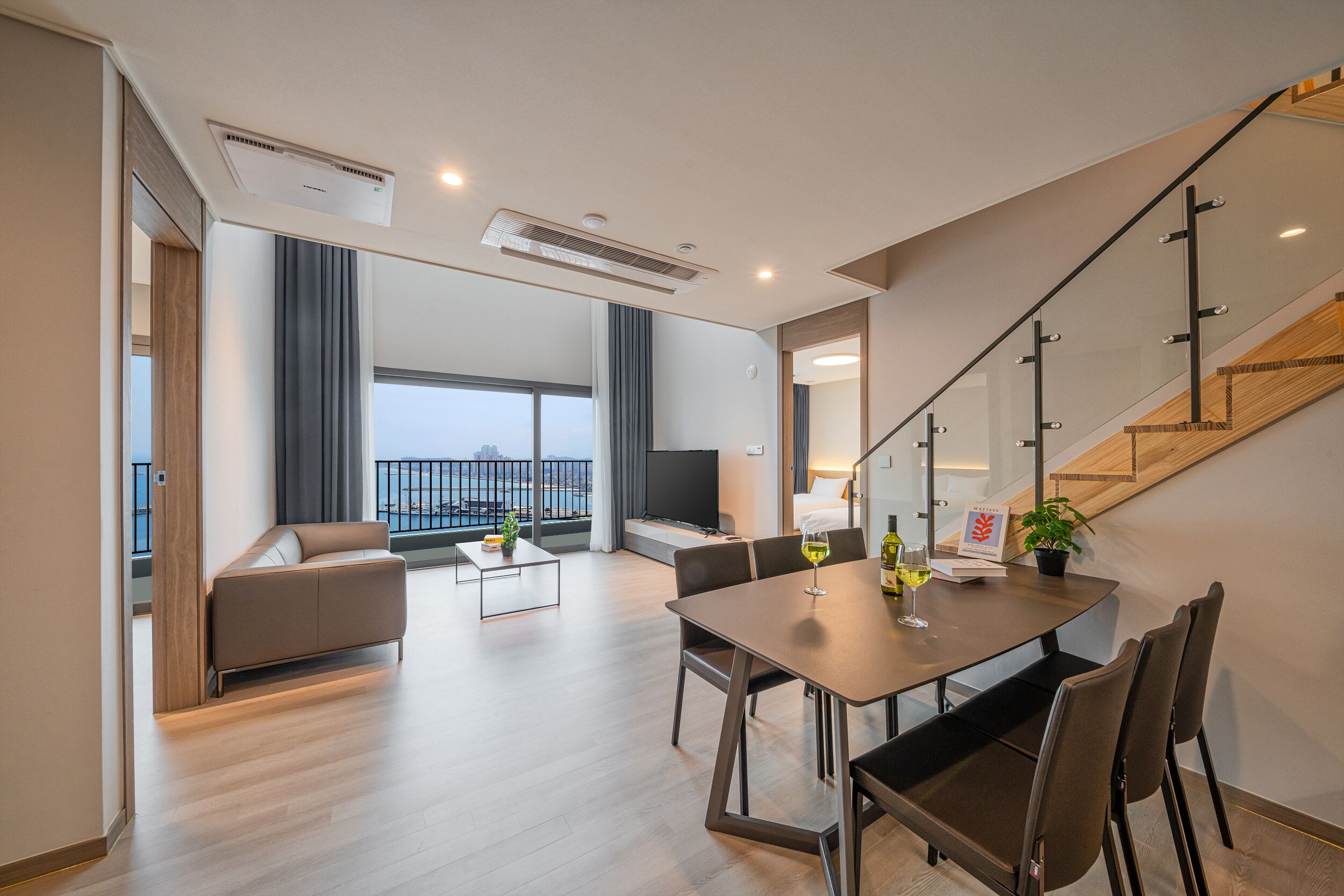 Una sala de estar moderna con un sofá, una mesa de comedor con sillas, un televisor y una escalera.