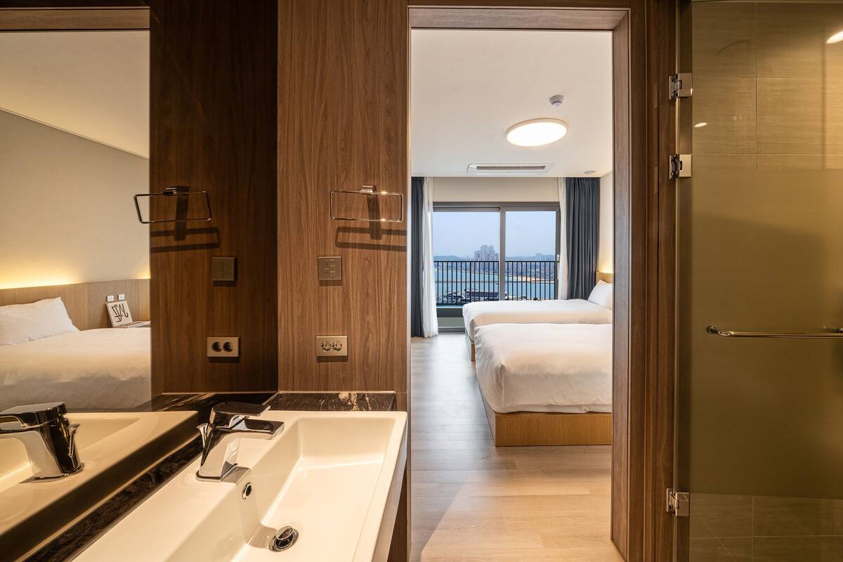 Habitación de hotel con un baño amplio, dos camas y vistas a la ciudad.