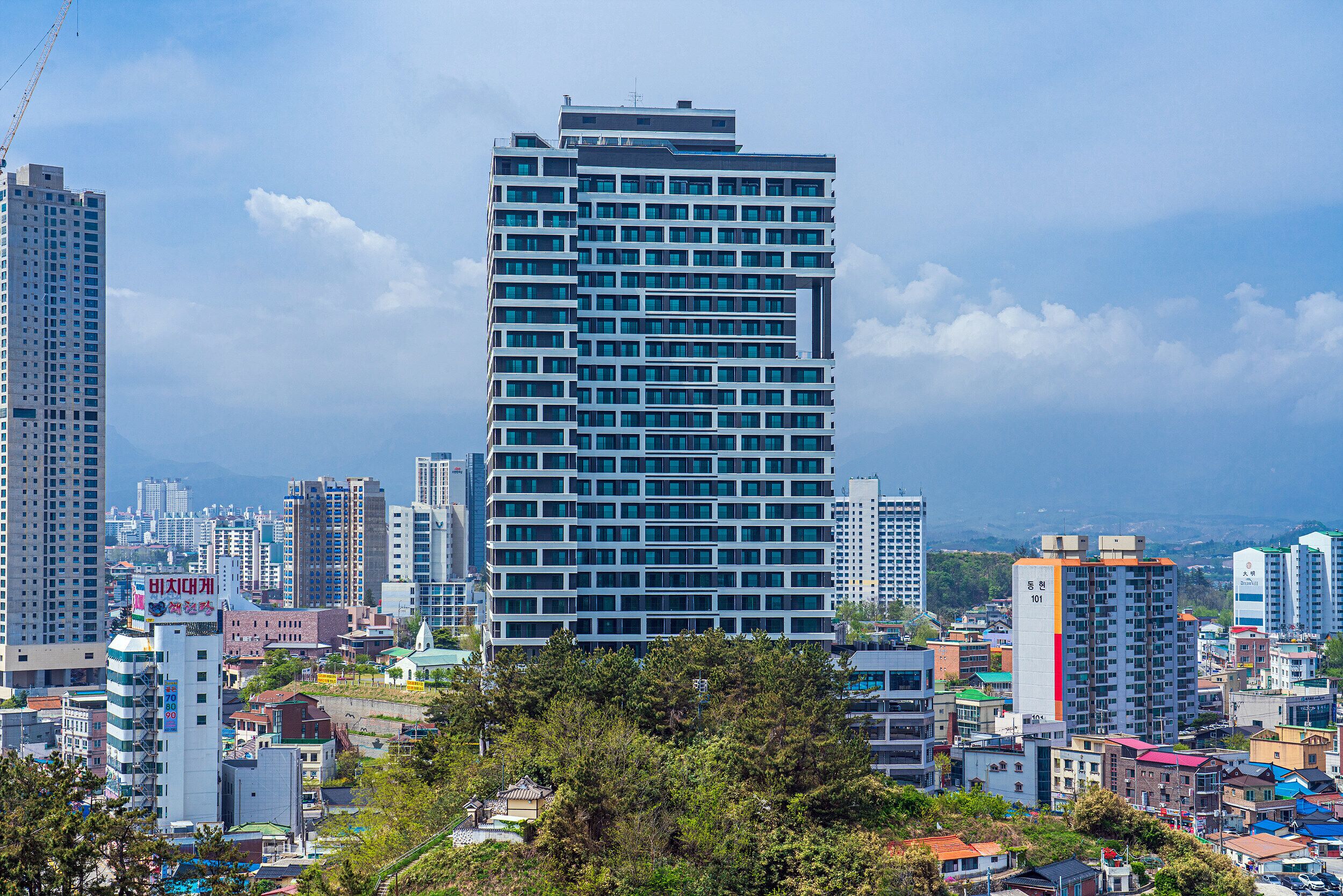 A high-rise building with a modern design, surrounded by other buildings and greenery.