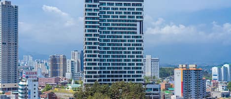 A high-rise building with a modern design, surrounded by other buildings and greenery.