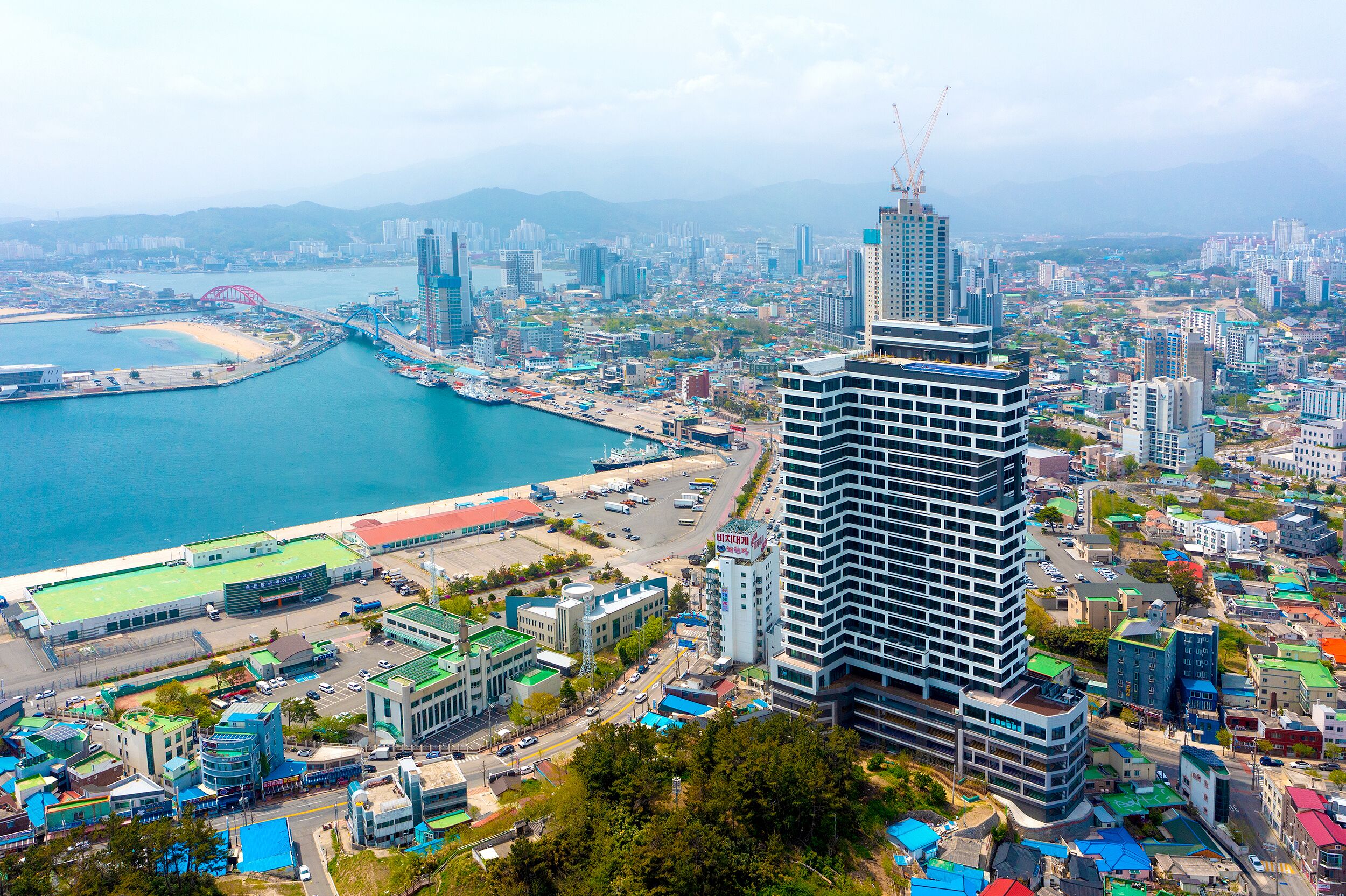 A cityscape with a prominent modern building, a coastal area with a bridge, and a mix of residential and commercial buildings.