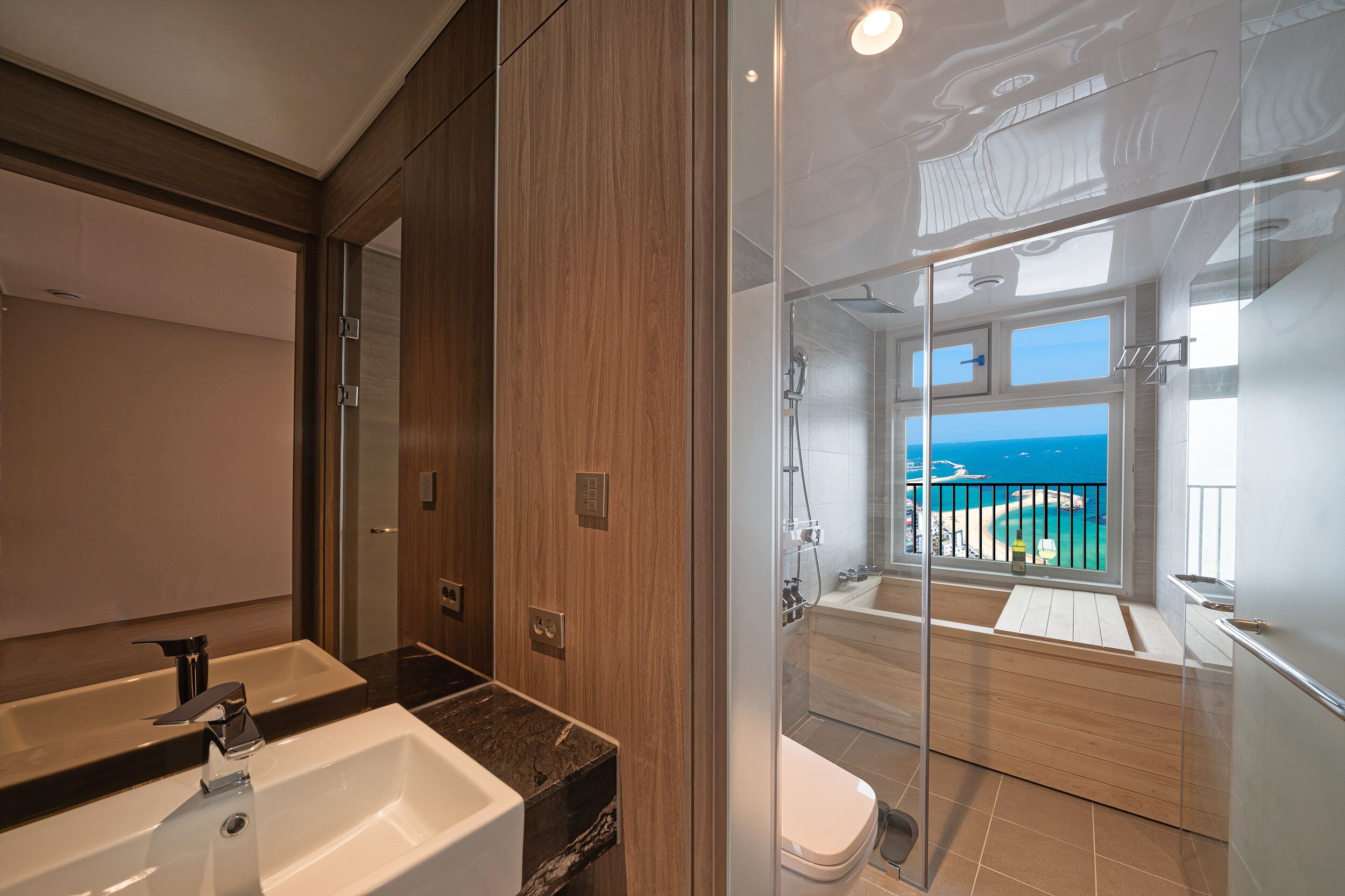 Une salle de bain moderne avec un grand miroir, un lavabo et une douche séparée par une paroi de verre.