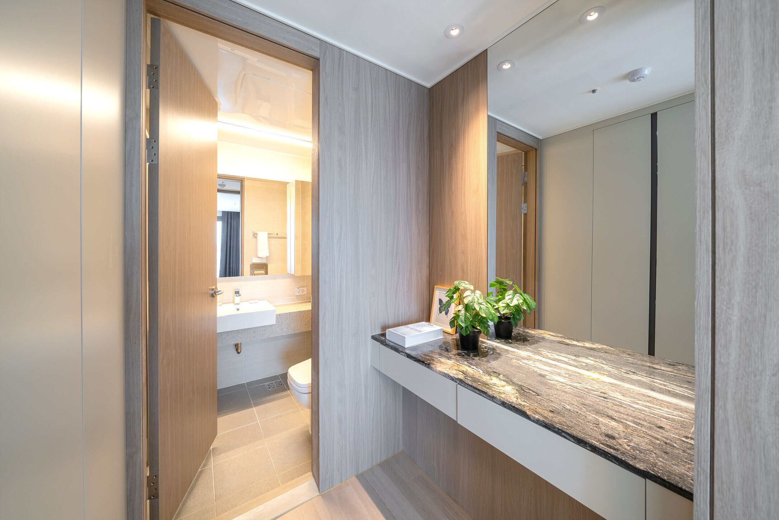 A modern bathroom with a wooden vanity, a large mirror, and a potted plant.