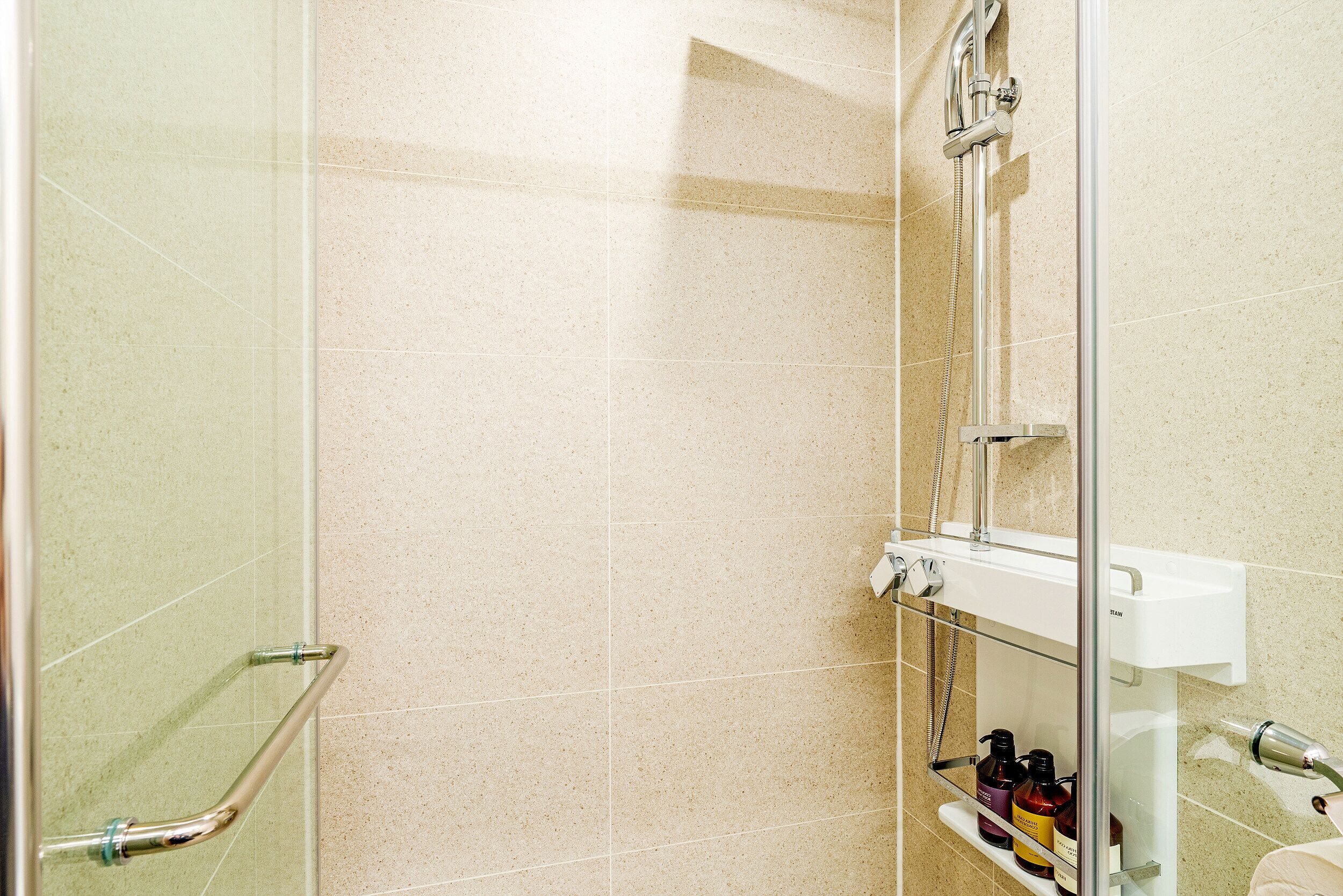 A shower area with a glass door, a handrail, and a shelf with toiletries.