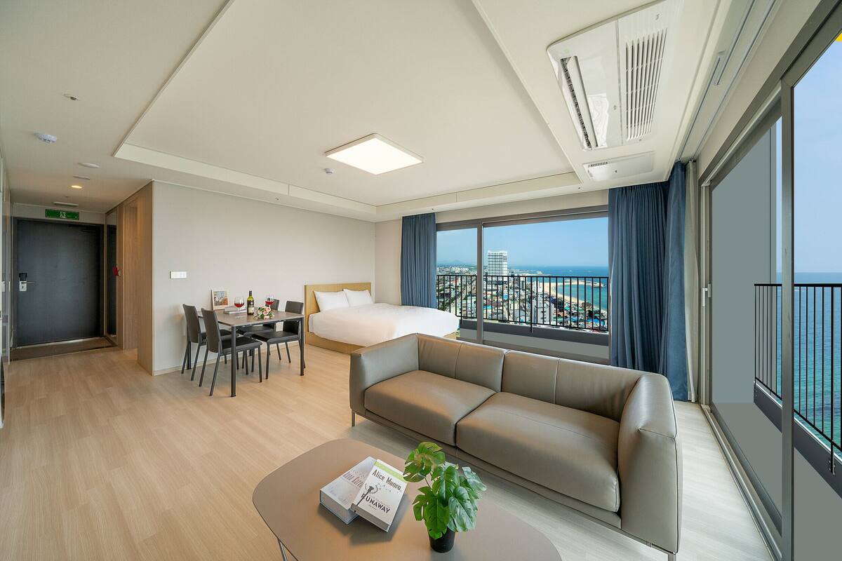 Una habitación de hotel moderna con cama, sofá, mesa de comedor y vista al mar.