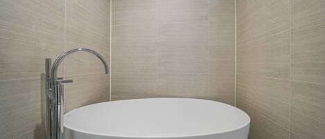 Une salle de bain moderne avec une baignoire sur pieds, des accessoires chromés et des murs recouverts de carreaux de couleur claire.