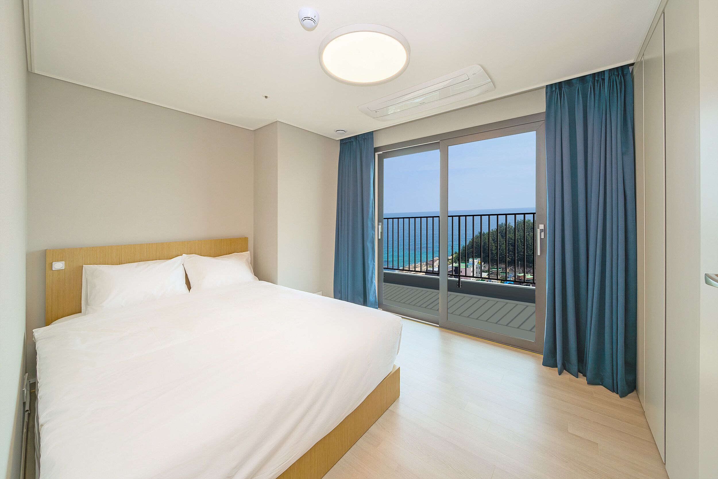 Une chambre d’hôtel avec un grand lit, un balcon donnant sur la mer et un luminaire au plafond.