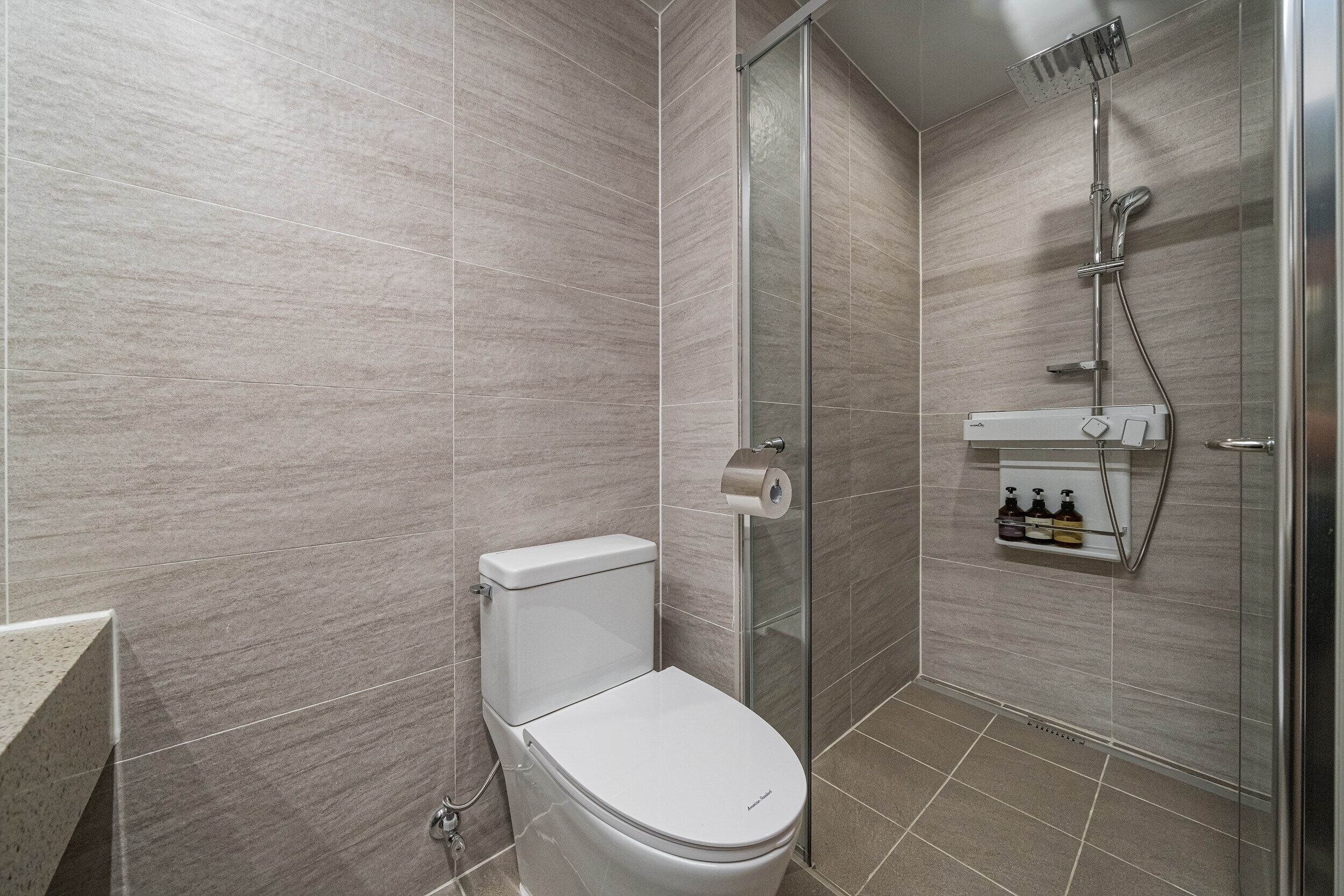 Un baño moderno con inodoro, cabina de ducha de vidrio y estante para dispensador de jabón.