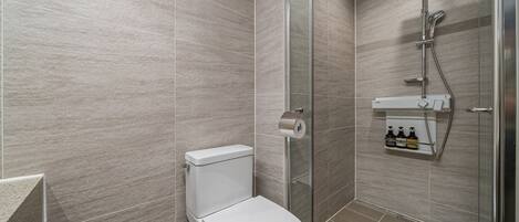 Un baño moderno con inodoro, cabina de ducha de vidrio y estante para dispensador de jabón.